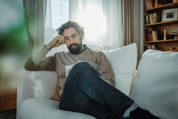 Fototapeta premium Man relaxing on sofa reading book at home