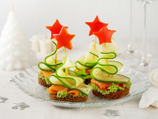 Festive Christmas fir tree canape with smoked salmon, star pepper and rye bread against  backdrop of festive served family dinner on light background of bokeh lights.