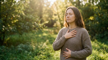 Woman meditating and practicing deep breathing, standing outdoors in a sunny green forest, mindfulness and spiritual well-being concept.