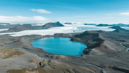 Aerial view of a turquoise glacial lake surrounded by rugged terrain and distant ice fields under a clear blue sky