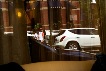 American City Life: Street Scene Reflection in Shop Window Showing SUV, Historic Brick Building, and Patriotic Flags