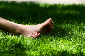 Outdoor Leisure: Bare Feet with Red Toenails Relaxing on Green Grass in Summer Nature Close-up