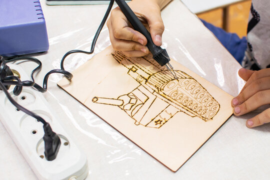 Top view of childs hands using a burning tool to trace patterns on a wood board. Inspiring creative pyrography activity for children. Artistic creative hobby for kids.