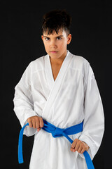 Karate student adjusting karate belt and posing in white uniform on dark backdrop. Emphasizes alignment, preparation, and clean martial arts form.