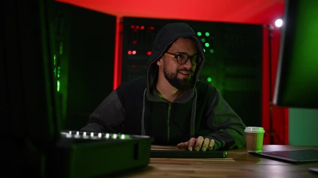 Hooded hacker typing code in a data center server room