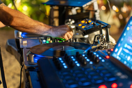 Primer plano de mano de DJ mezclando m&uacute;sica en tocadiscos de vinilo y mesa de mezclas digital en club nocturno con luces azules.