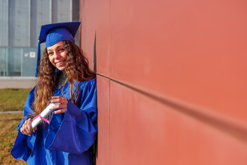 Young woman wearing cap and gown, holding her diploma with a proud smile
