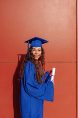 Female student celebrating academic achievement, holding diploma and wearing a graduation cap and gown