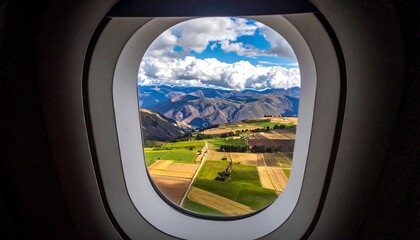 Fototapeta premium View from plane window of patchwork fields and mountains under a cloudy blue sky on a sunny day