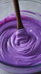 Vibrant purple paint mixed in glass bowl with wooden spoon