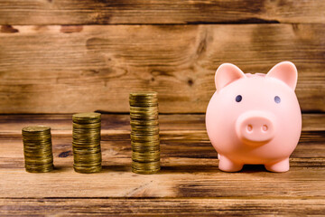 Pink piggy bank and stacks of the coins on wooden background