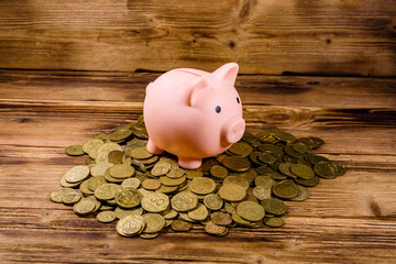 Pink piggy bank and pile of the ukrainian coins on wooden background