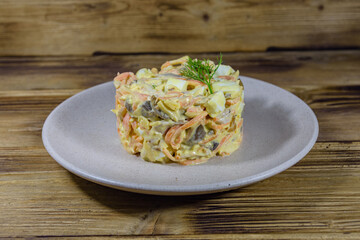 Salad with chicken breast, marinated mushrooms, carrot, eggs, boiled potato and mayonnaise on a wooden table