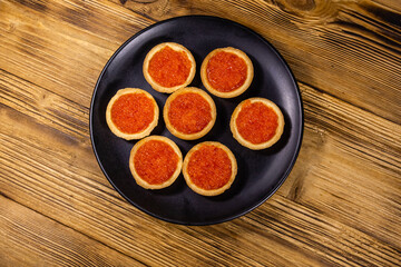 Tartlets with red caviar on a black plate. Festive food. Top view