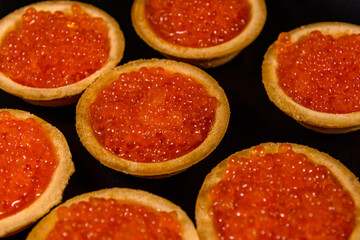 Tartlets with red caviar on a black plate. Festive food