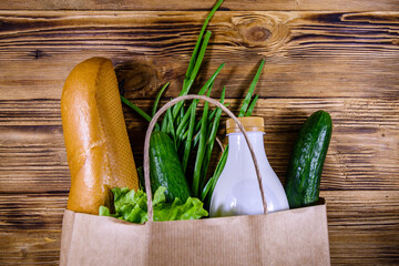 Paper bag with different food from grocery on a wooden table. Supermarket shopping concept. Top view