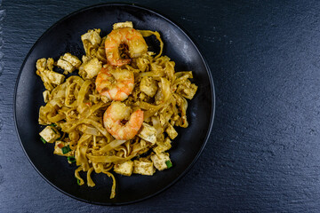 Black plate with pad thai on a slate board. Top view