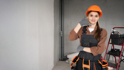 Woman Builder. female Architect in work overalls and hardhat showing call me and phone gesture in...