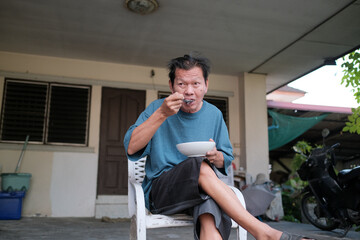 Fototapeta premium A man is eating a bowl of food while sitting on a chair