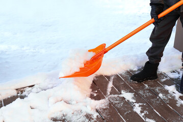 Removing a lot of snow by orange plastic shovel from wooden terrace