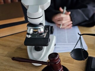 Microscope and gavel on desk in legal setting with papers and scales of justice