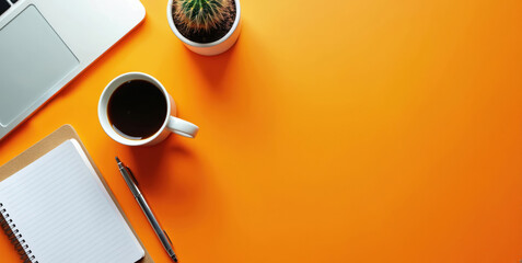 Top view of bright orange desk with laptop notebook pen and coffee cup. Cactus adds green accent to colorful workspace. Modern office setup for productive work and planning.