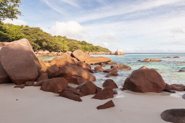 Sunlit tropical beach scene with large red boulders along a white sandy shore,