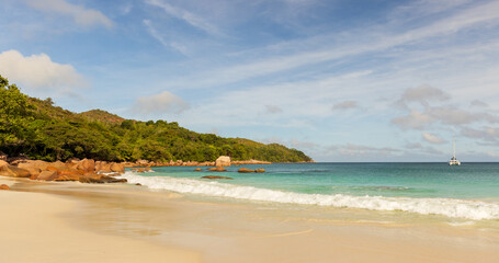 A sunny tropical beach scene with golden sand, gentle waves and rocky shoreline