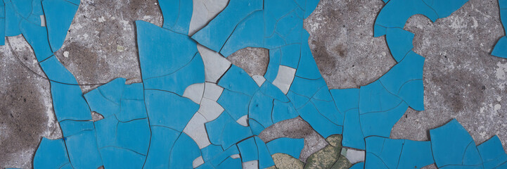 Peeling paint on the wall. Panorama of a concrete wall with old cracked flaking paint. Weathered rough painted surface with patterns of cracks and peeling. Wide panoramic grunge texture for background