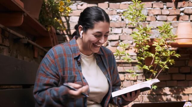 Laughing woman with planner in hands having video call with her colleagues. She turning pages and starting reading aloud new company goals