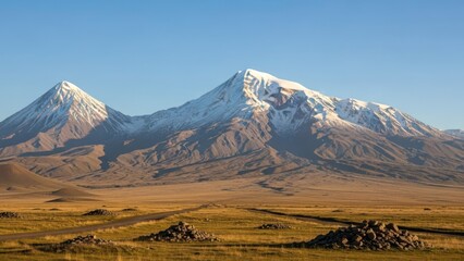 A breathtaking landscape of snow-capped mountains rising above a vast, open valley under a clear blue sky.