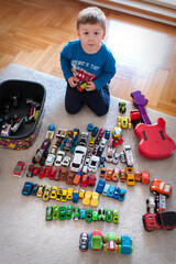 A child sits on the floor, organizing toy cars into rows. A guitar lies nearby while the sun shines through a window, adding light to the room.