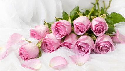 Fototapeta premium Pink roses bouquet with soft petals and green leaves arranged on white fabric background for romantic floral concept