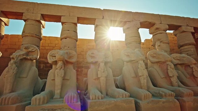 Row of ancient ram headed sphinx statues aligned in front of massive stone columns inside the Karnak Temple