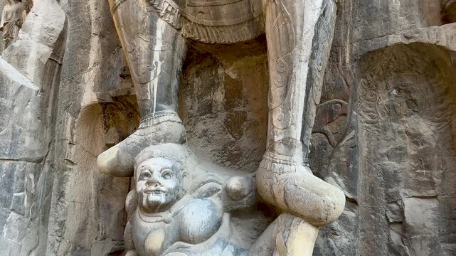 Statues of Vaisravana (Northern Heavenly King) and demon or evil spirit trampled underfoot on northern side of Fengxian Temple Cave at Longmen Grottoes, Luoyang, Henan, China. UNESCO World Heritage.