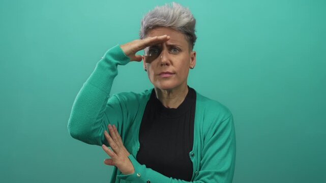 Woman shielding eyes with hand and crossing left arm over torso in studio setting; curiosity exploration.