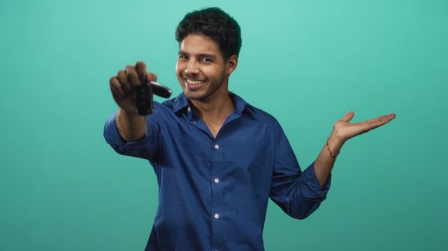Man holding car keys with palm up gesture in studio, smiling and offering keys; confidence invitation sale.