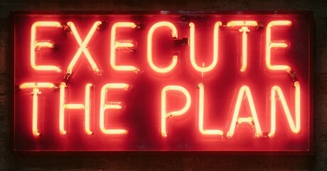 Bright red neon sign displays text. Words execute the plan glow against dark brick wall. Dramatic lighting creates strong visual impact.