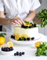 Person decorates a lemon cream cake with fresh blackberries and mint leaves