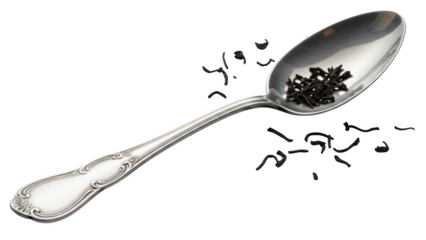 Antique silver spoon holding loose black tea leaves with scattered leaves on black background loose leaf tea
