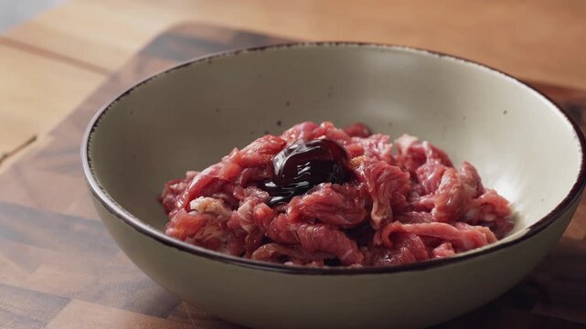 Chef cutting raw beef with knife on wooden cutting board - meat preparation process in kitchen