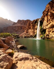 Picturesque waterfall cascading into a serene pool, framed by rocky cliffs under a clear blue sky