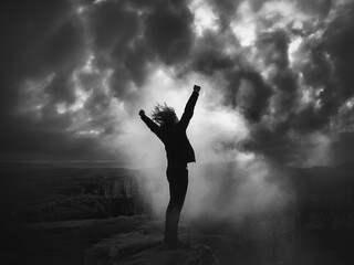 Silhouette of a person with arms raised against stormy sky