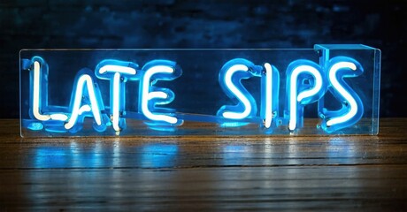 Bright neon sign displays Late Sips. Blue glow illuminates clear acrylic block resting on wood surface. Dark background enhances contrast.