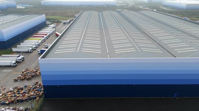 Panning aerial view of huge ombre clad industrial distribution centre, logistics and transport hub retailers and manufacturers in Milton Keynes, UK. 