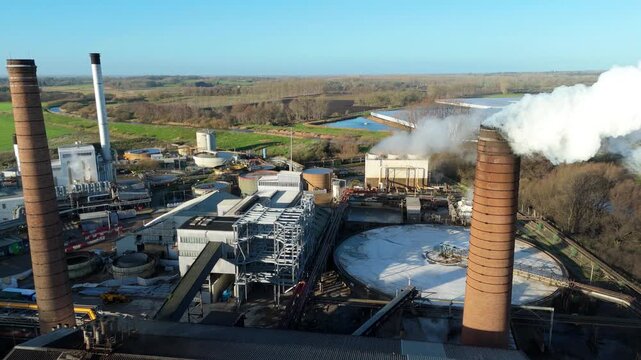 Close up aerial drone view of smoke stack chimney spewing smoke plumes at industrial factory site, sugar beet processing and production, Wissington, UK.