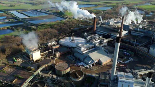 Aerial drone view of large scale industrial factory, sugar beet production processing facility, smoke from chimneys and clarifying tanks for used water cooling, Wissington, United Kingdom.