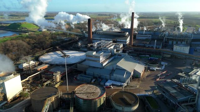 Aerial drone view of large scale industrial factory, sugar beet production processing facility, smoke from chimneys and clarifying tanks for used water cooling, Wissington, United Kingdom.