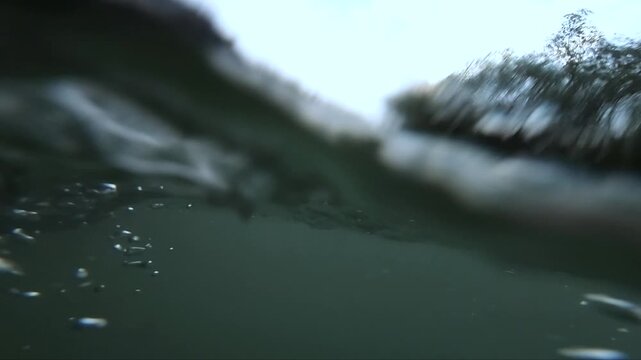 Underwater hands and oars creating ripples in clear water surface