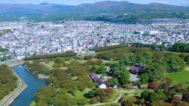 Panoramic aerial footage overlooking the star-shaped Goryokaku Fort park surrounded by moat and dense trees with cityscape and distant mountains from Goryokaku Tower in Hakodate Hokkaido Japan.